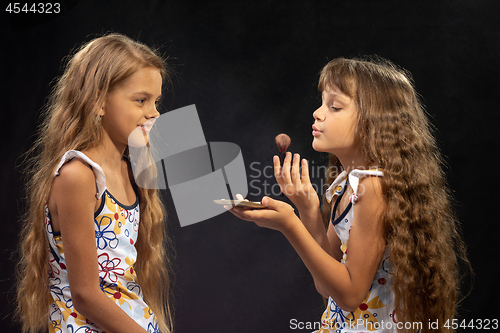 Image of A girl blows on a brush with powder, another girl looks closely at her closely