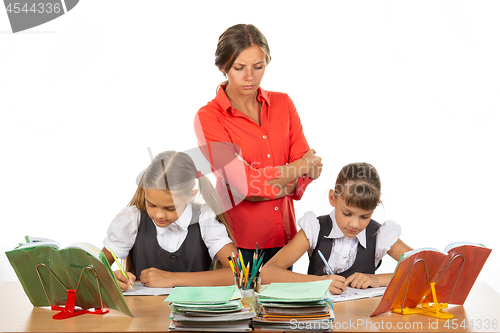 Image of A strict teacher stands above the children who solve the task