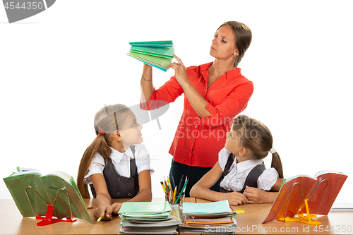 Image of The teacher considers the notebooks of students, two schoolgirls look at her with interest