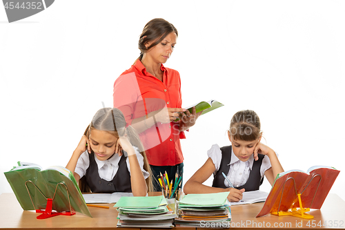 Image of Schoolchildren at the desk do the assignment, the teacher in the background reads the assignment