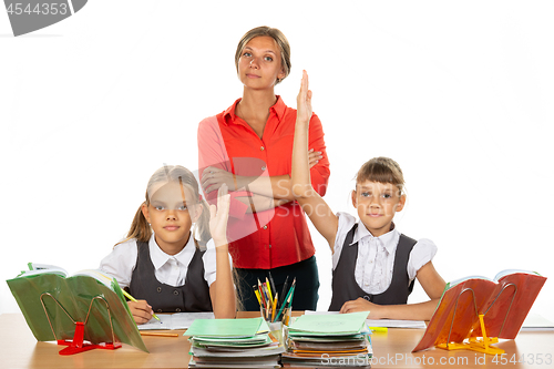 Image of Children pull their hands up, ready to answer a question, in the background a satisfied teacher