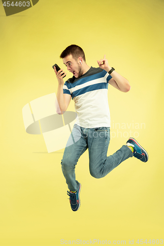 Image of Full length portrait of happy jumping man with gadgets on yellow background