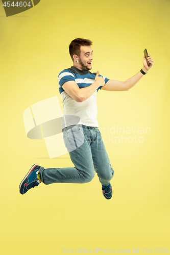 Image of Full length portrait of happy jumping man with gadgets on yellow background