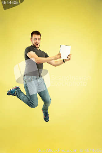 Image of Full length portrait of happy jumping man with gadgets on yellow background