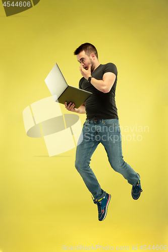 Image of Full length portrait of happy jumping man with gadgets on yellow background