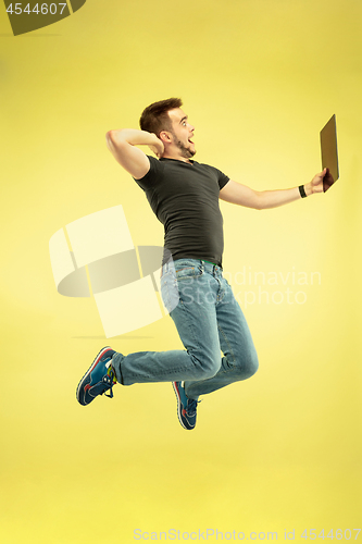 Image of Full length portrait of happy jumping man with gadgets on yellow background