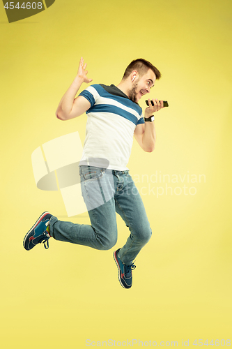 Image of Full length portrait of happy jumping man with gadgets on yellow background