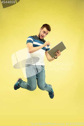 Image of Full length portrait of happy jumping man with gadgets on yellow background