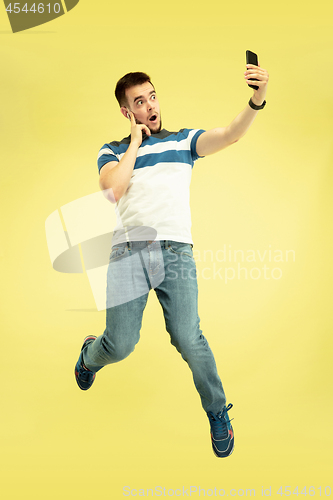 Image of Full length portrait of happy jumping man with gadgets on yellow background