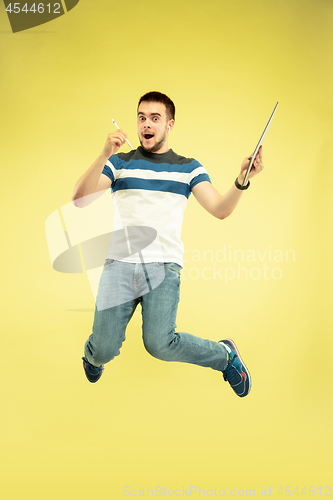 Image of Full length portrait of happy jumping man with gadgets on yellow background