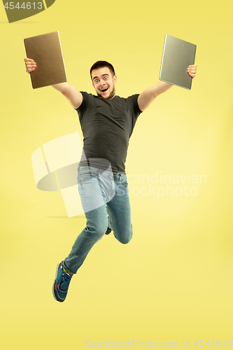 Image of Full length portrait of happy jumping man with gadgets on yellow background