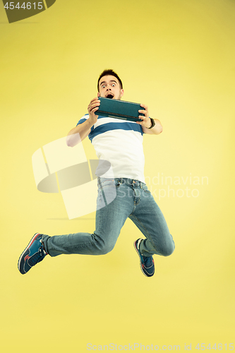 Image of Full length portrait of happy jumping man with gadgets on yellow background
