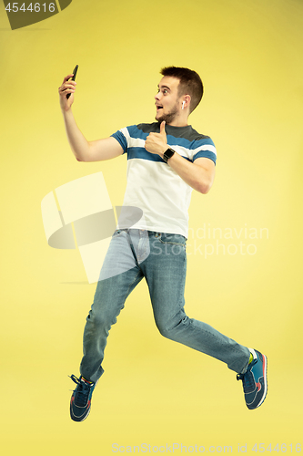 Image of Full length portrait of happy jumping man with gadgets on yellow background