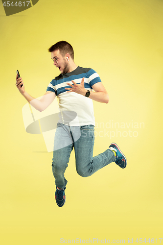 Image of Full length portrait of happy jumping man with gadgets on yellow background