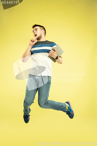 Image of Full length portrait of happy jumping man with gadgets on yellow background