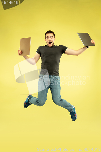 Image of Full length portrait of happy jumping man with gadgets on yellow background