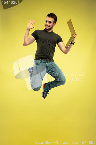 Image of Full length portrait of happy jumping man with gadgets on yellow background