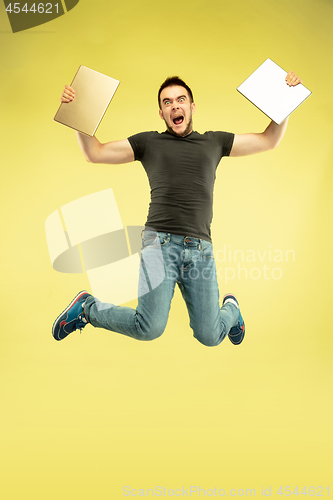 Image of Full length portrait of happy jumping man with gadgets on yellow background