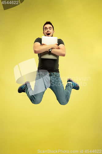 Image of Full length portrait of happy jumping man with gadgets on yellow background