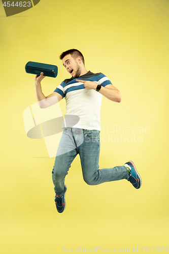 Image of Full length portrait of happy jumping man with gadgets on yellow background