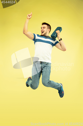 Image of Full length portrait of happy jumping man with gadgets on yellow background