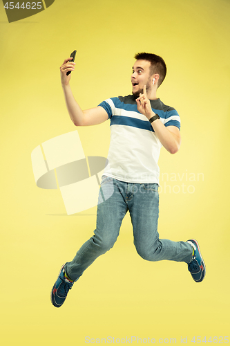 Image of Full length portrait of happy jumping man with gadgets on yellow background
