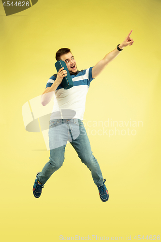 Image of Full length portrait of happy jumping man with gadgets on yellow background