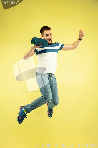 Image of Full length portrait of happy jumping man with gadgets on yellow background