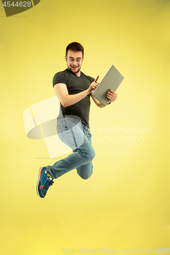 Image of Full length portrait of happy jumping man with gadgets on yellow background