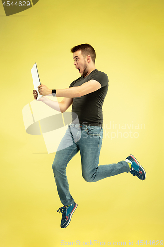 Image of Full length portrait of happy jumping man with gadgets on yellow background