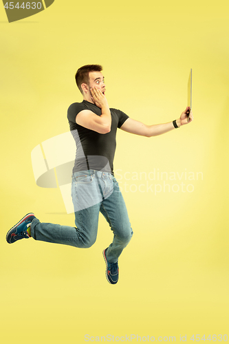 Image of Full length portrait of happy jumping man with gadgets on yellow background