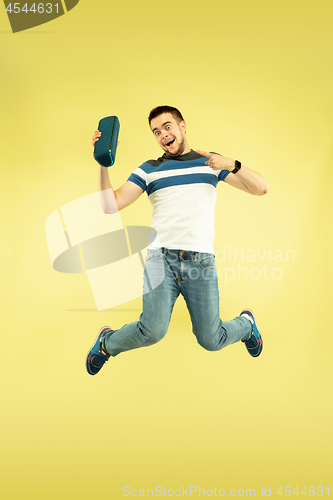 Image of Full length portrait of happy jumping man with gadgets on yellow background