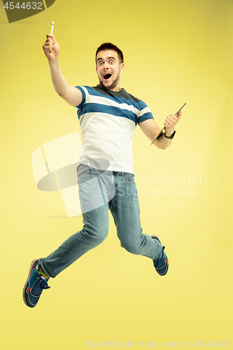 Image of Full length portrait of happy jumping man with gadgets on yellow background