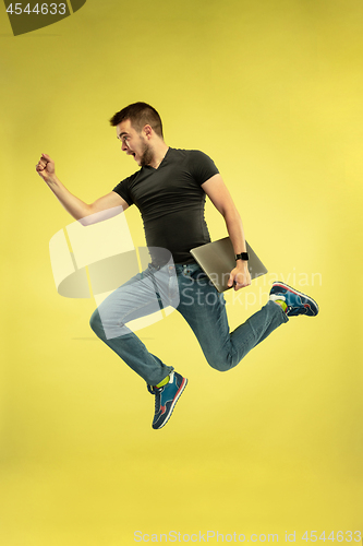 Image of Full length portrait of happy jumping man with gadgets on yellow background