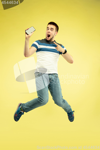 Image of Full length portrait of happy jumping man with gadgets on yellow background