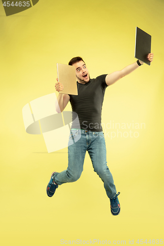 Image of Full length portrait of happy jumping man with gadgets on yellow background