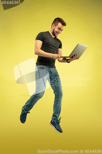 Image of Full length portrait of happy jumping man with gadgets on yellow background