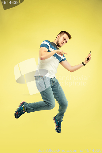 Image of Full length portrait of happy jumping man with gadgets on yellow background