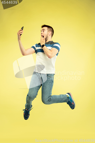 Image of Full length portrait of happy jumping man with gadgets on yellow background