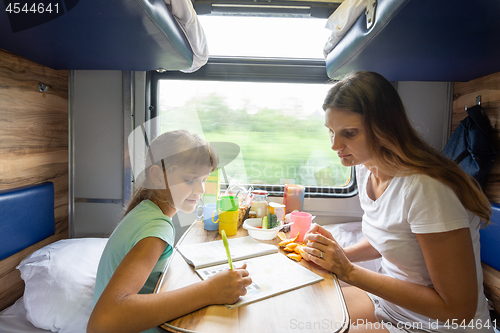 Image of Mom and daughter sit at the table in the train and solve the puzzle in the children\'s magazine