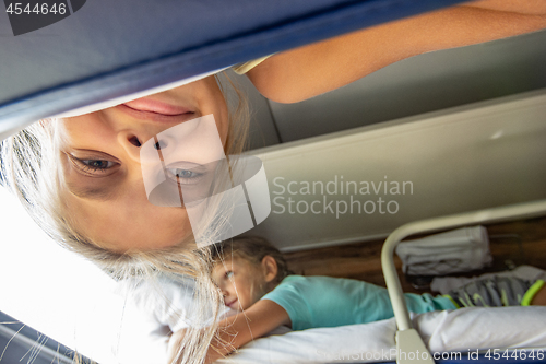 Image of A girl hanging from the top shelf in a train looks into the frame