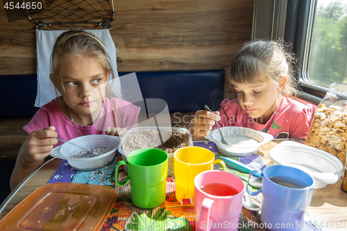 Image of Two girls eat buckwheat with milk from plastic disposable tableware on a train
