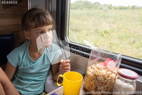 Image of The girl eats cookies on the train and looks out the window