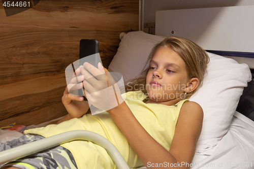 Image of The girl lies on the top shelf in the carriage and plays in the smartphone