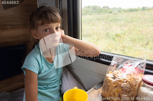 Image of A girl sitting in a reserved seat carriage in a train thoughtfully looks into the frame