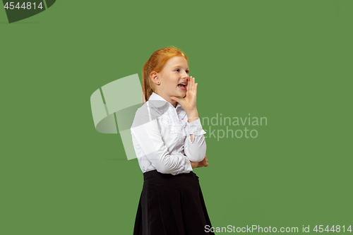 Image of The young teen girl whispering a secret behind her hand over green background