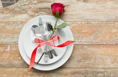 Image of red rose on set of dishes with cutlery on table