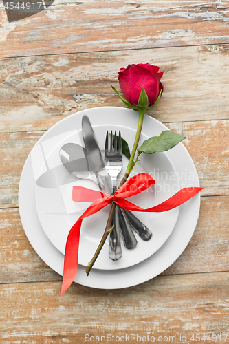 Image of red rose on set of dishes with cutlery on table