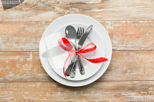 Image of cutlery tied with red ribbon on set of plates