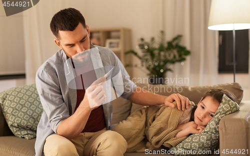 Image of father with thermometer and ill daughter at home